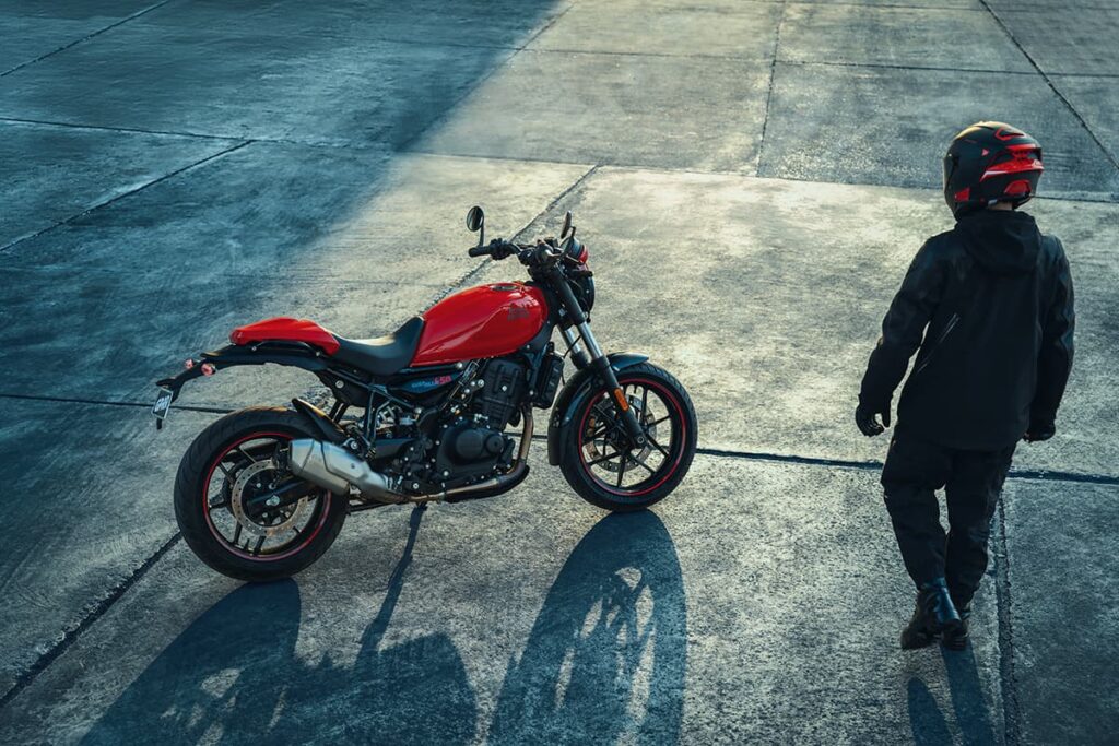 Eine rote Royal Enfield Guerrilla 450 APEX in Seitenansicht. Rechts daneben ein Motorradfahrer.