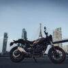 Eine Royal Enfield Guerilla 450 APEX in einer Seitenansicht vor einer Brücke und einer Skyline