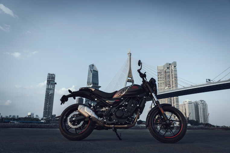 Eine Royal Enfield Guerilla 450 APEX in einer Seitenansicht vor einer Brücke und einer Skyline